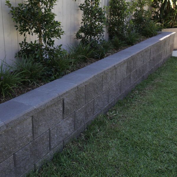 a concrete planter with plants in it next to a white wall and grass on the ground