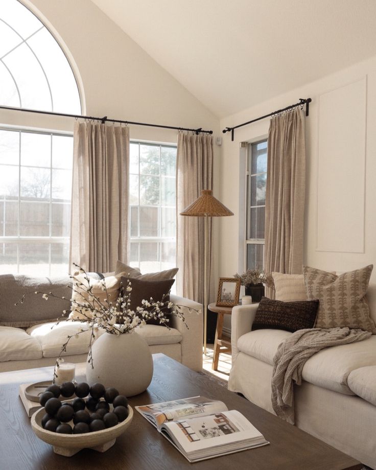 a living room filled with furniture and a large window covered in drapes, next to a coffee table