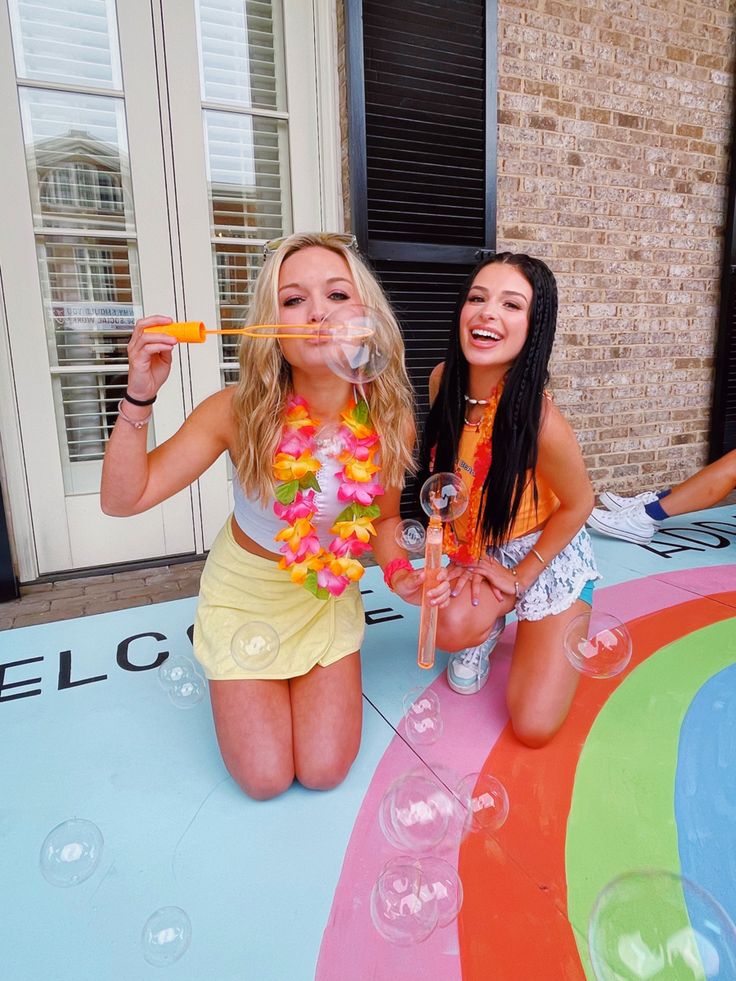 two young women sitting on the ground blowing bubbles