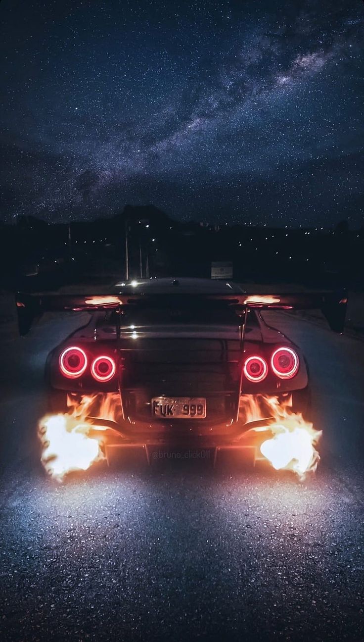 the back end of a sports car with its lights on at night in the dark