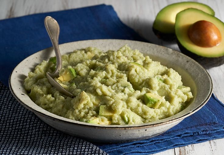 a bowl filled with mashed potatoes next to an avocado on a blue towel