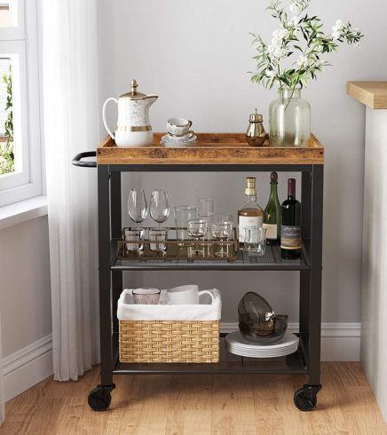 a bar cart with wine glasses, bottles and other items on it next to a window