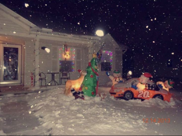 a house with christmas decorations on the front lawn and cars parked outside in the snow