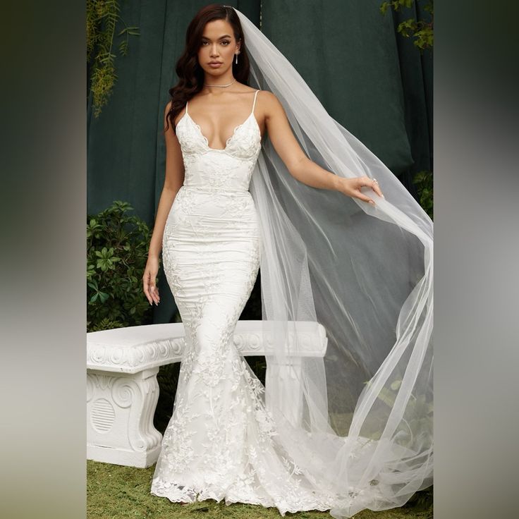 a woman in a wedding dress standing next to a bench with a veil over her head