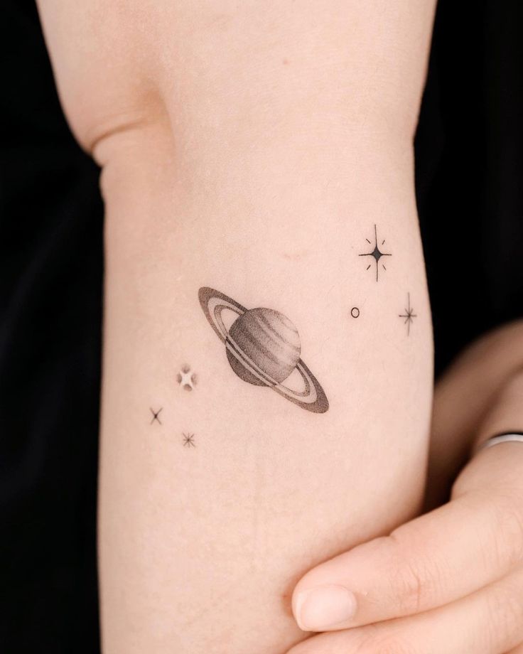 a small saturn tattoo on the right side of the arm, with stars around it