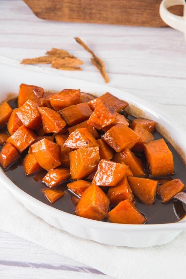 a white bowl filled with sweet potatoes on top of a wooden table next to cinnamon sticks