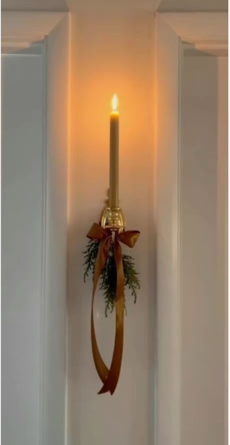 a lighted candle hanging on the wall next to a door with a ribbon around it