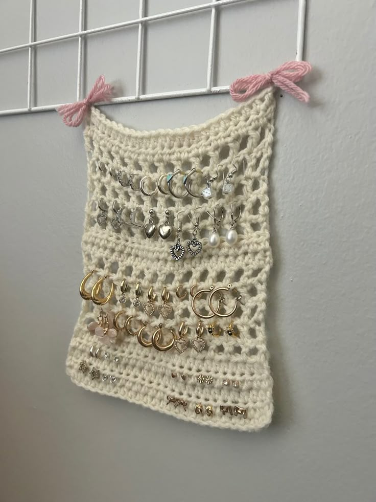 a white crocheted wall hanging with lots of rings and earring hooks attached to it