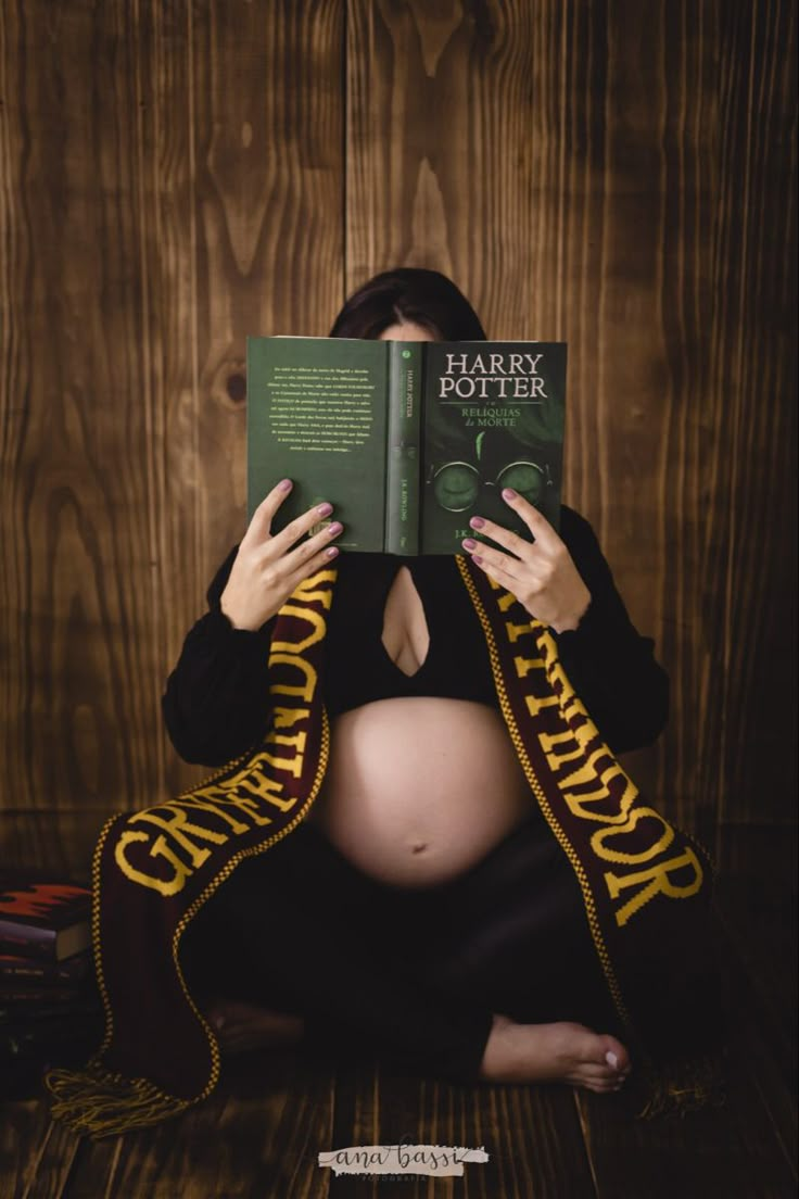 a pregnant woman sitting on the floor reading a harry potter book with her hands over her face