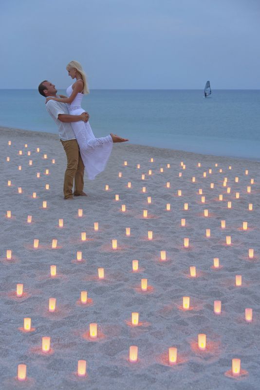 a man and woman standing on top of a sandy beach next to the ocean filled with floating candles