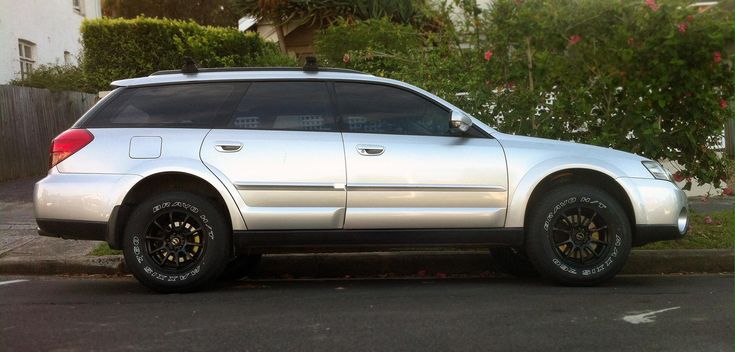 a silver car parked on the side of a road next to a tree and bushes