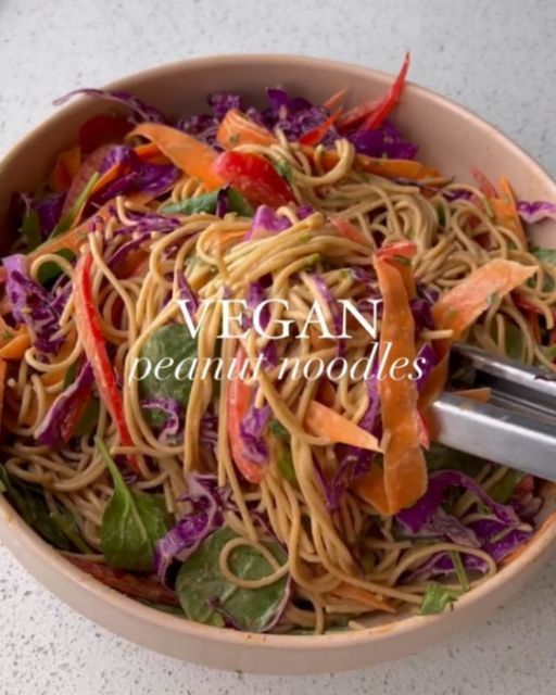 a bowl filled with noodles and vegetables on top of a white counter next to a pair of tongs