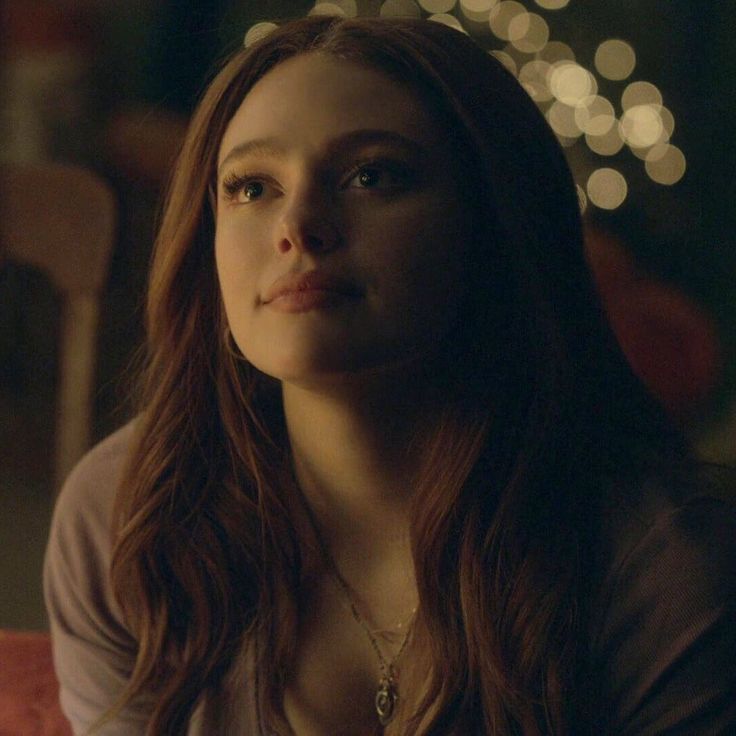 a woman with long hair sitting in front of a christmas tree and looking off into the distance