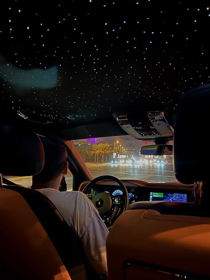 a man driving a car at night with stars on the ceiling and lights in the background