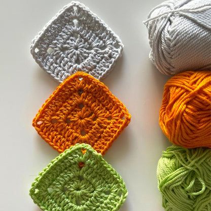 four balls of yarn sitting next to each other on top of a white surface with green and orange crocheted squares