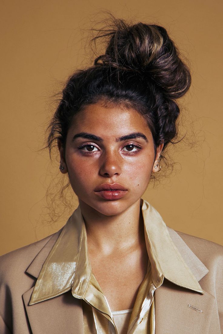 a woman in a beige suit and gold shirt with her hair pulled back into a bun