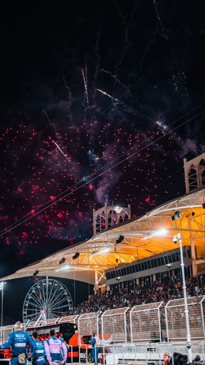 fireworks are lit up in the night sky above a crowd at a sporting event with people watching