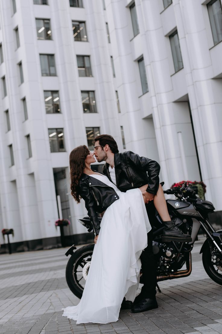 a bride and groom are sitting on a motorcycle in front of a large white building