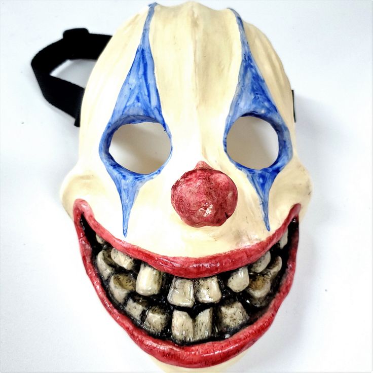 a clown mask with teeth and red nose on a white surface, it looks like he is smiling