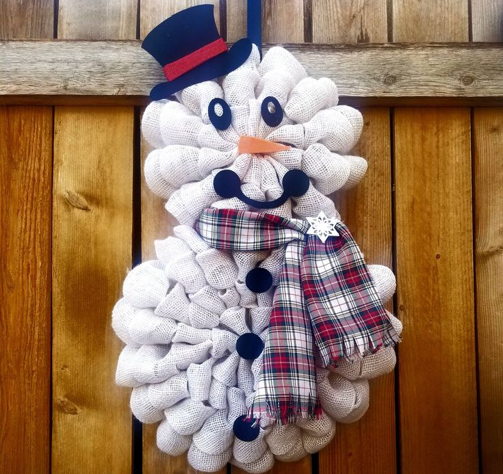 a snowman wreath hanging on the side of a wooden door with a hat and scarf