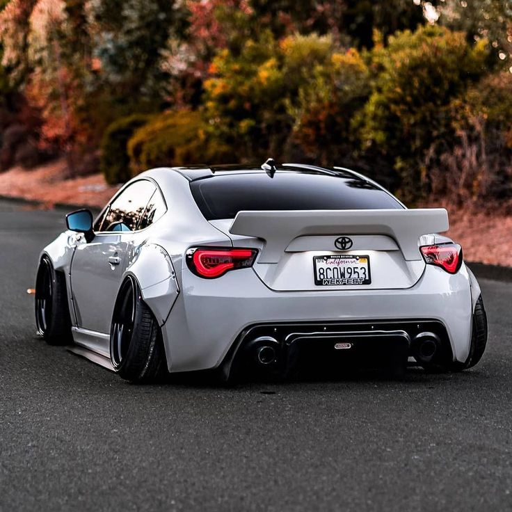 the rear end of a white sports car on a road with trees in the background