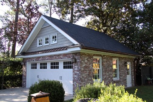 a house with two garages in front of it and bushes around the driveway area