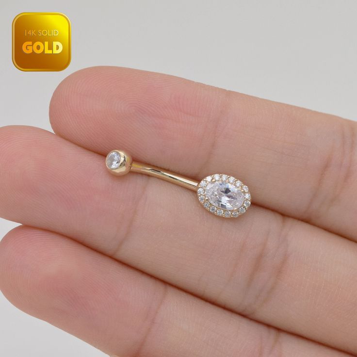 a person is holding a gold nose ring with an oval shaped diamond in the middle