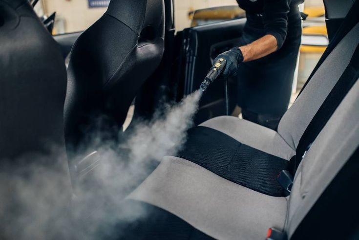 a man is cleaning the inside of a car with steam coming out of the passenger seat