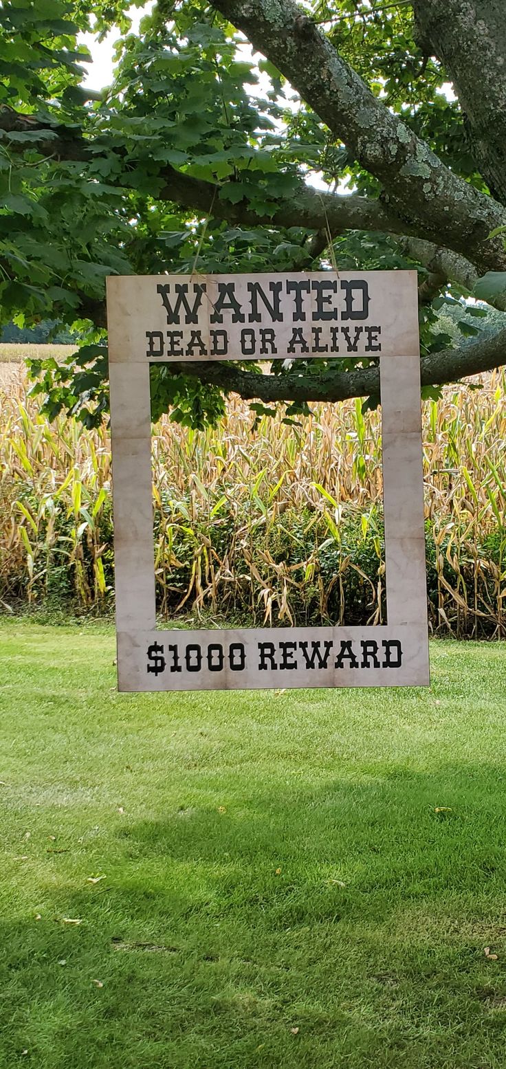 a sign that reads wanted dead or alive under a tree in front of a cornfield