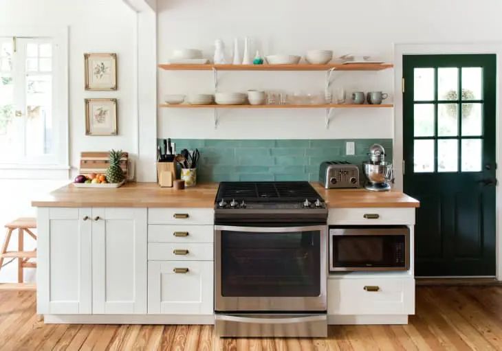 a kitchen with white cabinets and green tile backsplash, wood flooring and open shelving