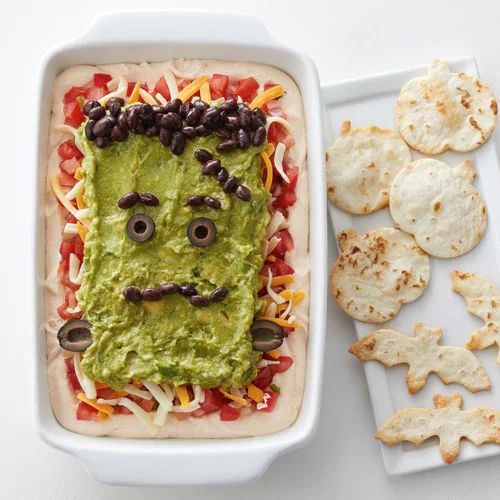 a white plate topped with guacamole and tortilla chips next to a tray of crackers