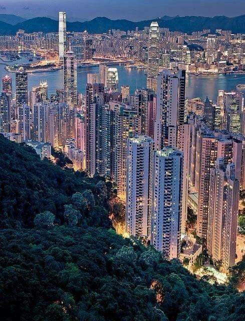 an aerial view of hong kong and the city lights at night, with mountains in the background