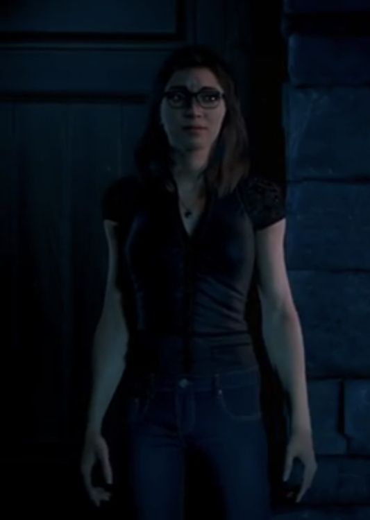 a woman with glasses standing next to a brick wall in the dark night, looking at the camera