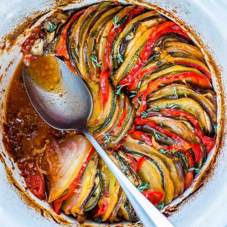 a white bowl filled with cooked vegetables and seasoning next to a spoon in it