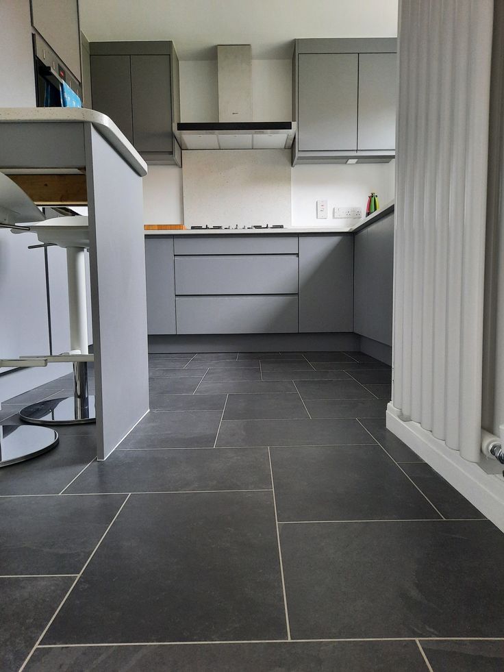 an empty kitchen with grey tile flooring and cabinets