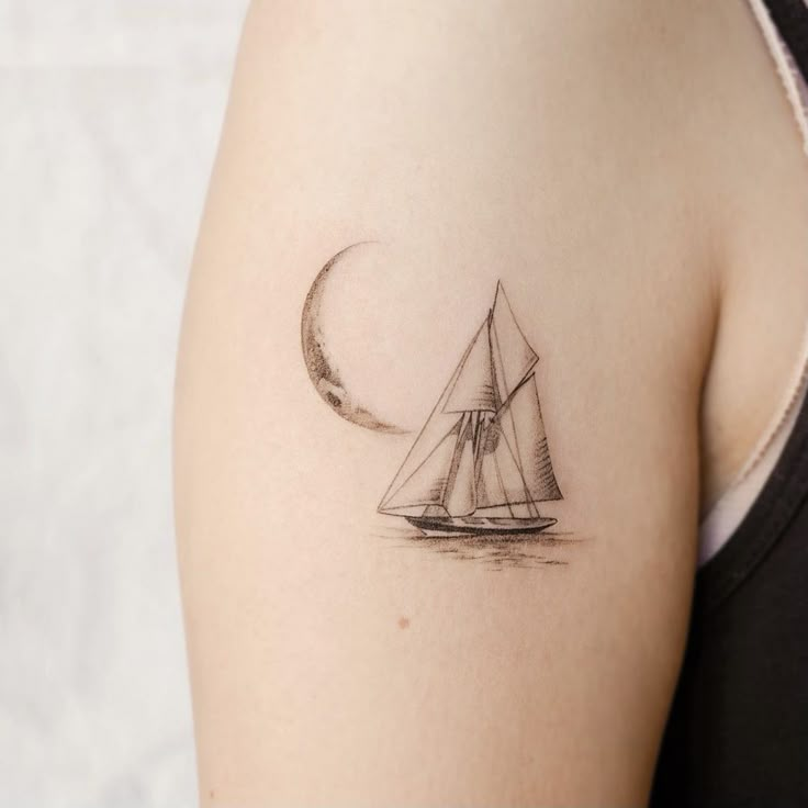 a small sailboat with a crescent moon tattoo on the back of her left arm