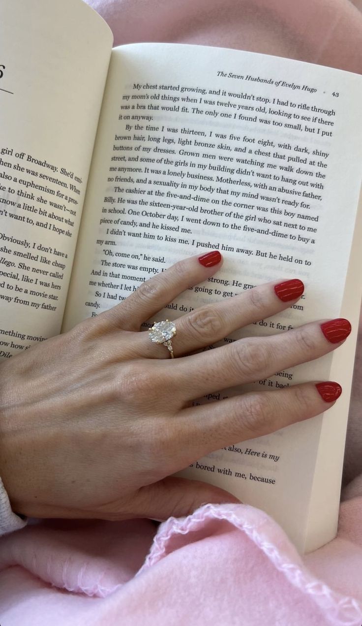 a woman's hand holding an open book and wearing a ring on her finger