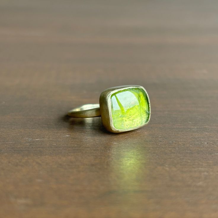 Judi Powers' signature corazon band serves as the pedestal for this vivacious peridot cabochon to rest on. 14k green gold Peridot 12mm x 10mm (1/2" x 7/16") Green Cabochon Ring Jewelry, Modern Yellow Gold Peridot Jewelry, Green Oval Cabochon Ring With Bezel Setting, Modern Green Peridot Jewelry, Modern Green Oval Cabochon Jewelry, Modern Green Cabochon Rings, Modern Green Cabochon Jewelry, 14k Gold Green Cabochon Jewelry, Modern Gold Jewelry With Peridot