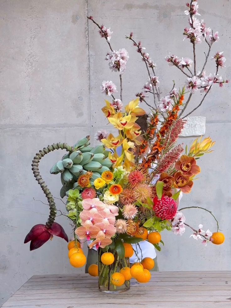 a vase filled with lots of different types of flowers and fruit on top of a wooden table