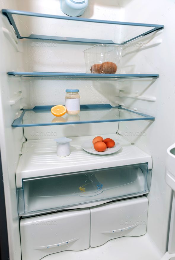 an empty refrigerator with some food on the shelf and one orange slice in front of it