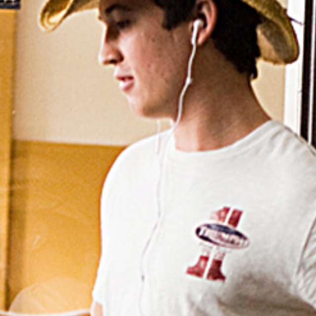 a young man wearing a hat and listening to music on his headphones while standing in front of a window