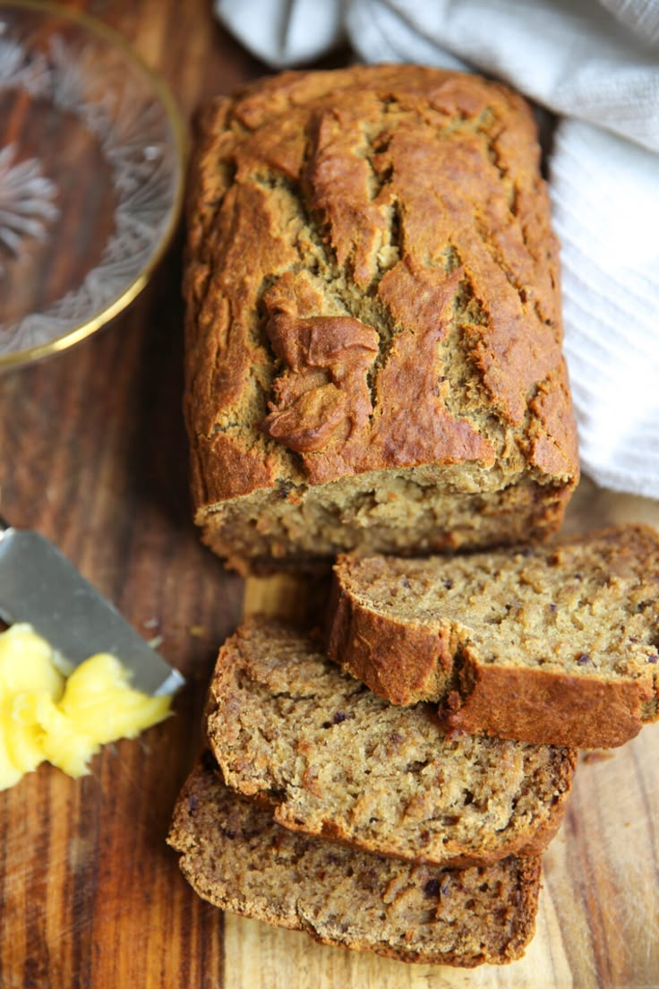 sliced loaf of banana bread sitting on top of a wooden cutting board next to butter