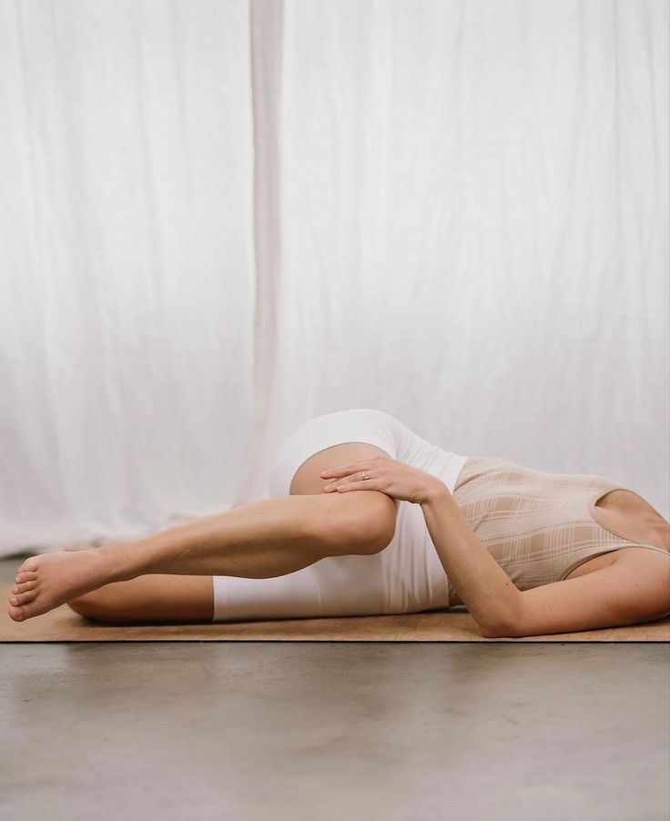 a woman laying on the floor with her arms behind her head and legs crossed, in front of a white curtain