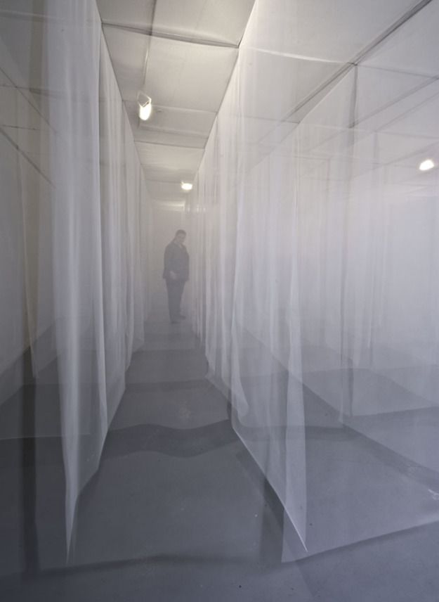 a man standing in the middle of a long hallway with sheer curtains covering it's walls