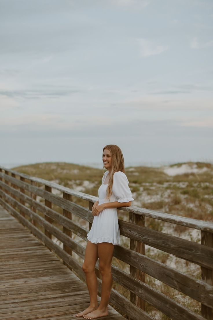 a woman standing on a boardwalk near the beach