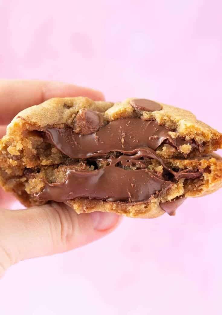 a hand holding a chocolate chip cookie with one bite taken out and the other half eaten