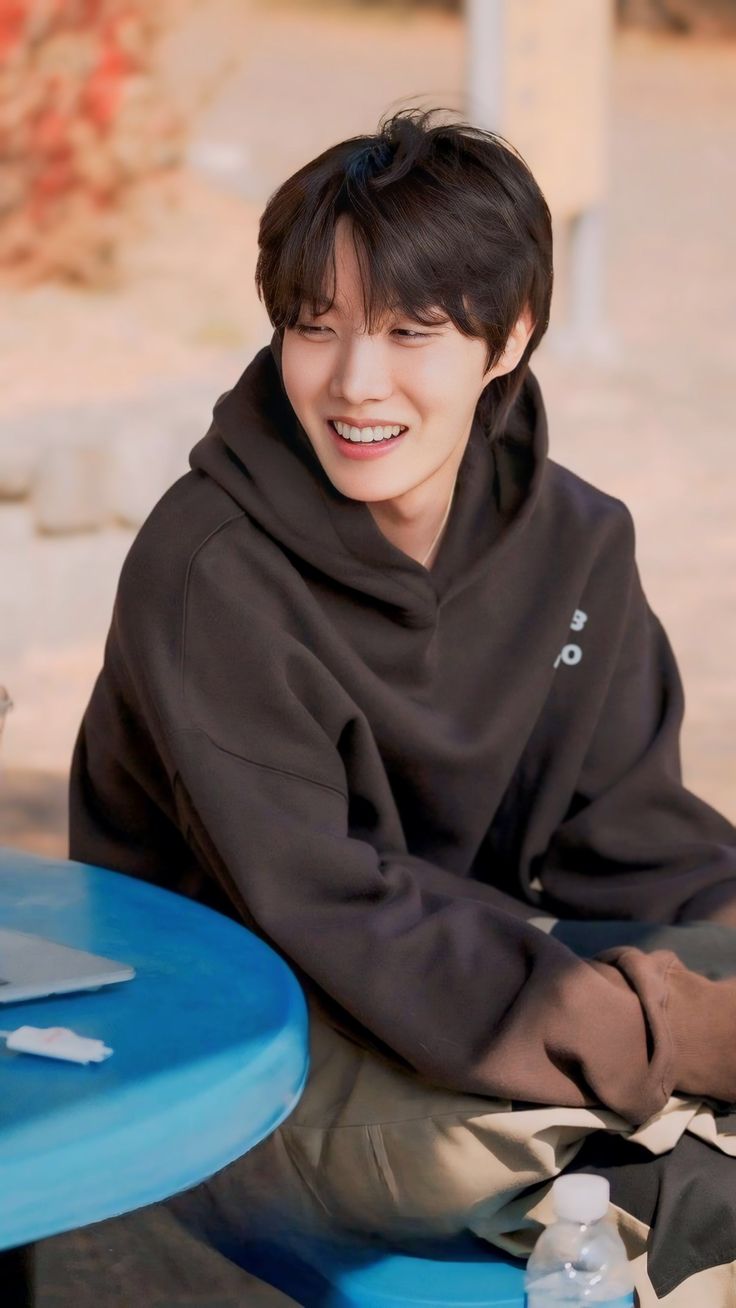 a young man sitting at a table with a smile on his face and wearing a black hoodie