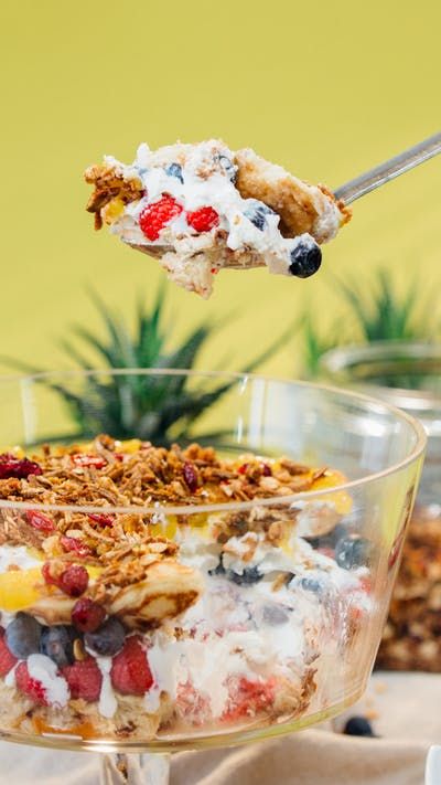 a spoon full of cereal with fruit and yogurt on top is being lifted from a glass dish