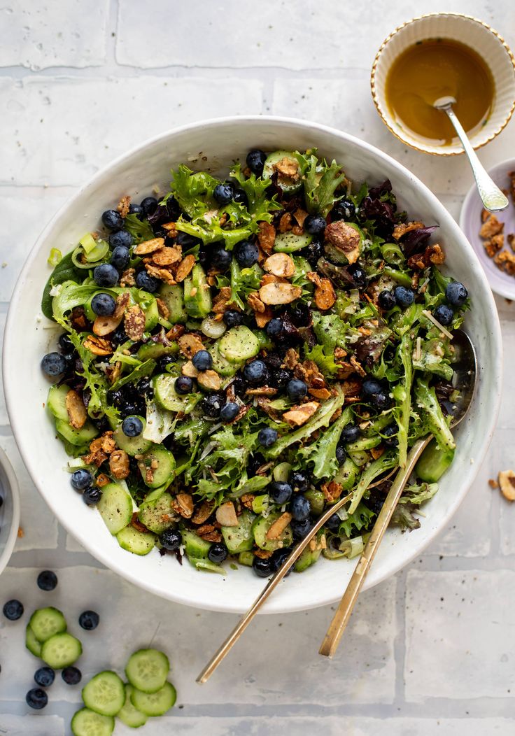 a white bowl filled with blueberries, cucumbers and nuts