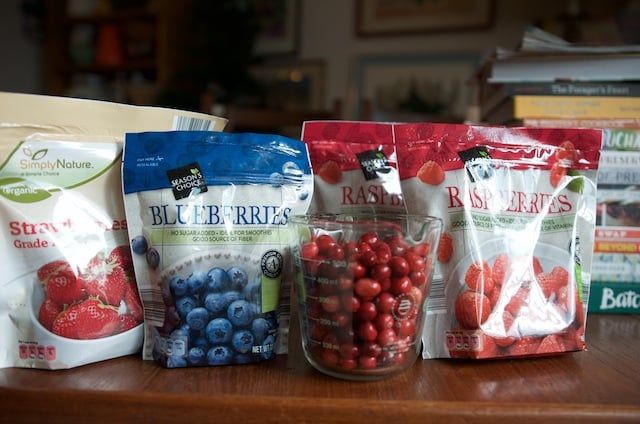 four bags of berries, blueberries and raspberries sit on a table in front of books